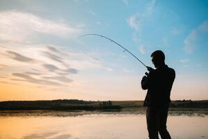 pêcheur homme pêche avec filage barre sur une rivière banque à brumeux brumeux lever du soleil. pêcheur avec filage. filage concept. photo