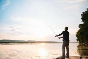 Jeune homme pêche à brumeux lever du soleil. photo