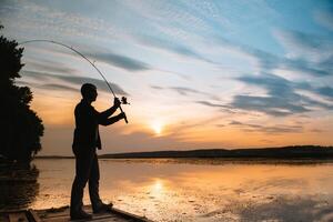 une pêcheur silhouette pêche à le coucher du soleil. eau fraiche pêche, capture de poisson. photo