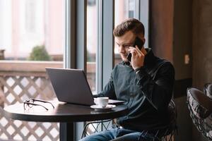 Jeune homme d'affaire parlant sur mobile téléphone tandis que travail sur portable dans café. photo