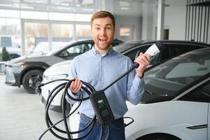 Jeune homme, vente électrique voitures dans le salle d'exposition. concept de achat respectueux de la nature voiture pour famille photo