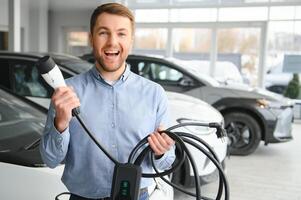 concept de achat électrique véhicule. Beau affaires homme des stands près électrique voiture à concession photo