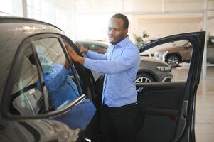 le sien rêver auto. content Jeune africain homme à la recherche excité choisir une voiture à le concession photo