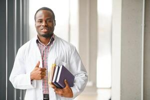 noir Masculin médecin étudiant portant une laboratoire manteau avec livre photo