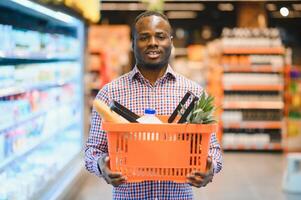 africain homme achats à supermarché. Beau gars en portant achats panier photo