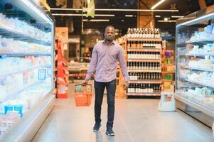 africain homme achats à supermarché. Beau gars en portant achats panier photo