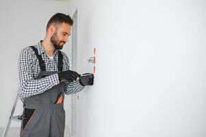 électricien dans uniforme montage électrique douilles sur le blanc mur à l'intérieur photo