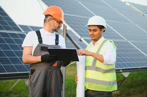 deux Masculin ingénieurs actuellement travail sur des plans à installer solaire panneaux à renouvelable solaire Puissance les plantes. ingénieur équipe pourparlers à propos installation solaire cellules sur rural zones photo