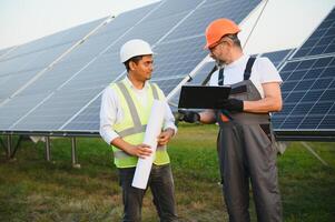 deux Masculin ingénieurs actuellement travail sur des plans à installer solaire panneaux à renouvelable solaire Puissance les plantes. ingénieur équipe pourparlers à propos installation solaire cellules sur rural zones photo