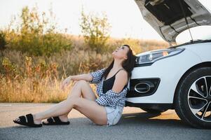 magnifique Jeune fille séance à une cassé voiture sur le route désespéré à avoir Aidez-moi photo