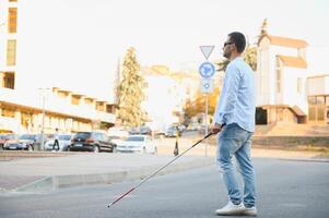 Jeune Beau aveugle homme en marchant avec bâton dans ville photo