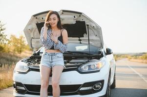 Jeune sexy femme avec cassé voiture appel sur le cellule téléphone. photo