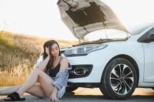 magnifique Jeune fille séance à une cassé voiture sur le route désespéré à avoir Aidez-moi photo