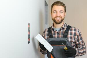 sur de soi professionnel électricien dans uniforme en utilisant Tournevis tandis que remplacer une prise dans appartement après rénovation travail. photo