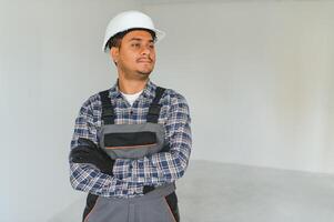 profession, construction et bâtiment - content souriant Indien ouvrier ou constructeur dans casque plus de gris Contexte. photo