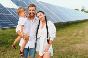 Jeune famille de Trois est accroupi près photovoltaïque solaire panneau, peu garçon et parents. moderne famille concept. le concept de vert énergie photo