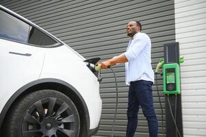 sérieux africain homme en portant charge câble dans sur main, permanent près luxe électrique auto. photo