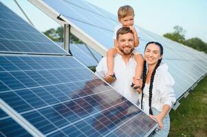 Jeune famille avec une petit enfant dans sa bras sur une Contexte de solaire panneaux. une homme et une femme Regardez à chaque autre avec l'amour. solaire énergie concept. photo