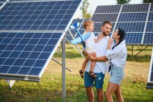 une large coup de une content famille permanent ensemble et souriant à caméra avec une grand solaire panneau dans Contexte photo