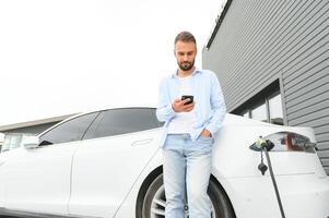 magnifique Jeune élégant homme est avec électrique voiture à jour mise en charge le véhicule photo