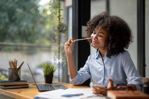 affaires femme séance et recherche information à plan, en pensant à propos travail, fourré une crayon dans sa joue tandis que pensée. photo