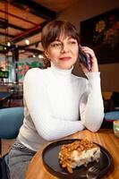 portrait de souriant femme parlant sur téléphone tandis que séance dans café, le déjeuner Pause photo