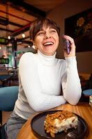 portrait de une largement en riant femme parlant sur le téléphone tandis que séance dans une café, le déjeuner Pause photo