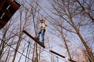 une garçon dans une casque grimpe une corde parc dans le printemps photo