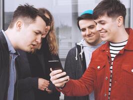 Jeune homme montrant quelque chose marrant sur le sien téléphone intelligent à une groupe de adolescent copains photo