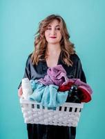 femme au foyer heureuse tenant un panier de vêtements prêts pour la lessive isolé sur fond bleu photo