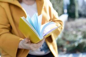 une femme dans une Jaune manteau détient une retournement carnet photo