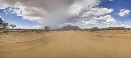 panoramique image plus de une gravier route dans damaraland pendant le pluvieux saison avec orage des nuages photo