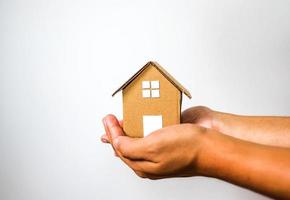 modèle de maison brune à 2 mains humaines sur fond blanc. concept d'investissement et de dette dans la maison. photo