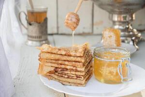 une homme verse mon chéri sur Crêpes et les boissons thé de une samovar, russe tradition de célébrer Maslenitsa photo