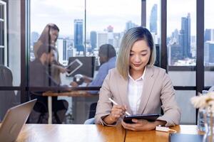 portrait de asiatique affaires PDG femme est travail dans Bureau à le table avec numérique tablette et montrant statistique graphique montrant annuel rapport et gratte-ciel Contexte photo