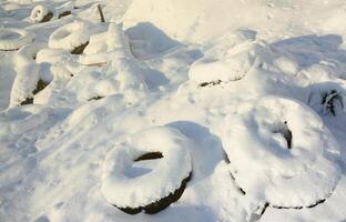 les pneus de voiture usagés et mis au rebut se trouvent sur le bord de la route, recouverts d'une épaisse couche de neige photo