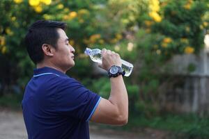 asiatique homme détient bouteille de en buvant l'eau à boisson Extérieur. concept, boisson l'eau pour bien santé. le soulagement de assoiffé, et protéger de chaleur accident vasculaire cérébral, cool vers le bas dans chaud temps condition. santé se soucier. photo