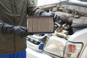 gros plan les mains du mécanicien tiennent le tampon de filtre à air du moteur de voiture pour vérifier. concept, voiture cassée, service de réparation et d'entretien. le filtre à air sale doit être changé pour être hygiénique. photo