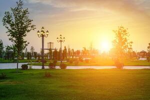 ville parc dans de bonne heure été ou printemps avec lanternes, Jeune vert pelouse, des arbres et spectaculaire nuageux ciel sur une le coucher du soleil ou lever du soleil. photo