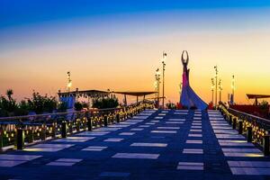 Ouzbékistan, Tachkent - avril 25, 2023 le territoire de le parc Nouveau Ouzbékistan avec monument de indépendance dans le forme de une stèle avec une humo oiseau à crépuscule. vue de une pont. photo