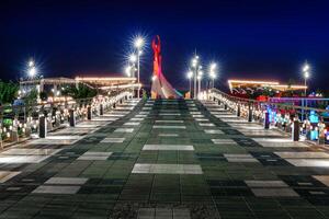 Ouzbékistan, Tachkent - avril 25, 2023 illuminé monument de indépendance dans le forme de une stèle avec une humo oiseau dans le Nouveau Ouzbékistan parc à la nuit. vue de le pont. photo
