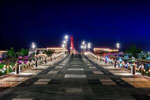 Ouzbékistan, Tachkent - avril 25, 2023 illuminé monument de indépendance dans le forme de une stèle avec une humo oiseau dans le Nouveau Ouzbékistan parc à la nuit. vue de le pont. photo