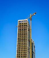 une grue bâtiment une moderne gratte-ciel contre une bleu ciel. construction placer. photo