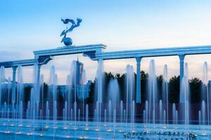 Mémorial et Lignes de fontaines illuminé par lumière du soleil à le coucher du soleil ou lever du soleil dans le indépendance carré à heure d'été, tachkent. photo