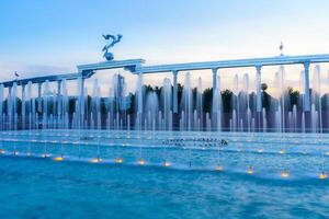 Mémorial et Lignes de fontaines illuminé par lumière du soleil à le coucher du soleil ou lever du soleil dans le indépendance carré à heure d'été, tachkent. photo