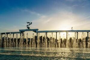 Mémorial et Lignes de fontaines illuminé par lumière du soleil à le coucher du soleil ou lever du soleil dans le indépendance carré à heure d'été, tachkent. photo