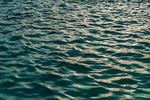 le texture de le vagues dans turquoise couleur, illuminé par le Soleil à le coucher du soleil ou aube. la nature Contexte. photo