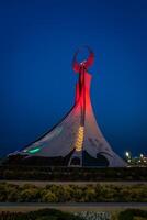 Ouzbékistan, Tachkent - mai 5, 2023 illuminé monument de indépendance dans le forme de une stèle avec une humo oiseau, fontaines et agitant drapeaux dans le Nouveau Ouzbékistan parc à la nuit. photo