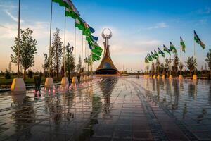 Ouzbékistan, Tachkent - mai 5, 2023 fontaines dans une Contexte de monument de indépendance dans le forme de une stèle avec une humo oiseau et agitant drapeaux sur une le coucher du soleil après pluie dans le Nouveau Ouzbékistan parc. photo