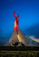 Ouzbékistan, Tachkent - mai 5, 2023 illuminé monument de indépendance dans le forme de une stèle avec une humo oiseau, fontaines et agitant drapeaux dans le Nouveau Ouzbékistan parc à la nuit. photo